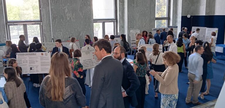 A crowd of people stand in a room with posters displayed on easels with a science fair feel to it.