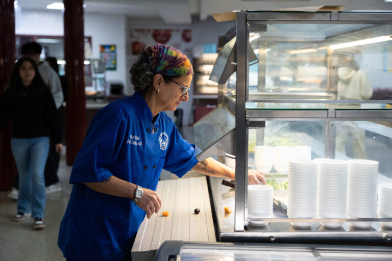 Great Valley School District culinary coordinator Jenifer Halin cleans up the salad bar in the cafeteria at Great Valley High School in Malvern, Pennsylvania. She is wearing a blue chef's coat and has a rainbow bandanna on her head.