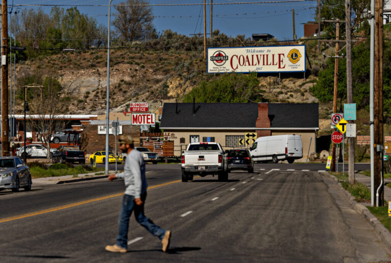A man crosses a street in a town with a billboard that says