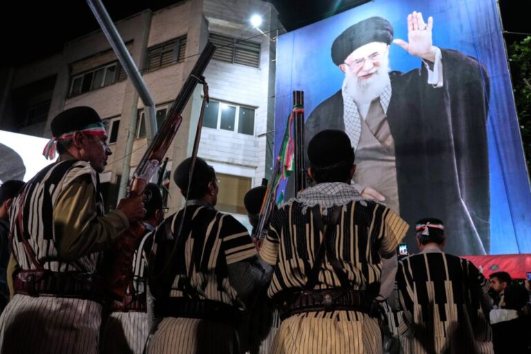Bakhtiari nomads, wearing traditional dress, hold their guns during a pro-government gathering near the residence where former Iranian Supreme Leader Ayatollah Ali Khamenei, shown on a banner, was killed in U.S. and Israeli strikes on Feb. 28, in Tehran, Iran, Monday, May 18, 2026. (AP Photo/Vahid Salemi)
