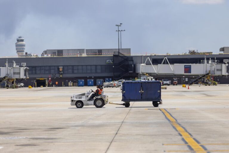 A Delta Air Lines employee drives an aircraft tug with a luggage cart on the tarmac at Atlanta Hartsfield Jackson International Airport.