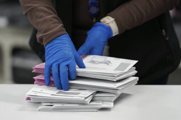 A closeup shows the gloved hands of an election worker sorting mail-in ballots.