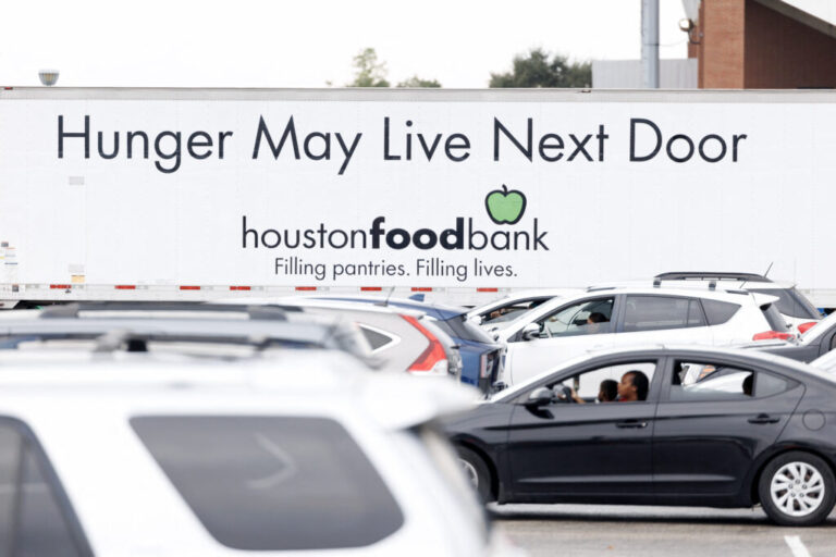 Cars with people inside are lined up at a food distribution event in Houston in November 2025. In the background is a large truck that says on its side: