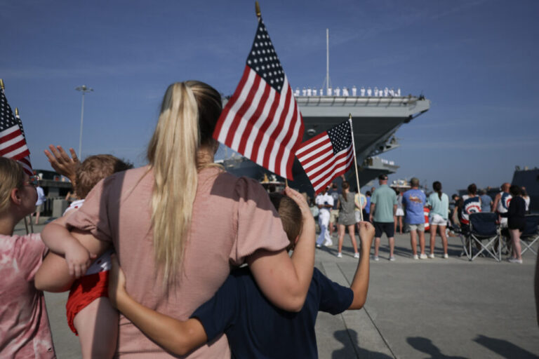 A woman stands with her children as her husband prepares to set sail on the aircraft carrier USS Gerald R. Ford from the Naval Station Norfolk on June 24, 2025, in Norfolk, Va. More than 10 months later the carrier and its crew is still at sea.