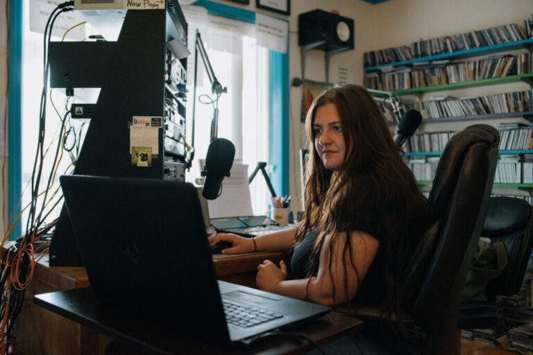 Abby DuFour, WCHG News Reporter and afternoon host of DuFour Du Jour, cues up the next song in her broadcast at station WCHG 107.1 FM, in Hot Springs, Virginia, on Friday, July 18th, 2025. Credit: Kristian Thacker for NPR