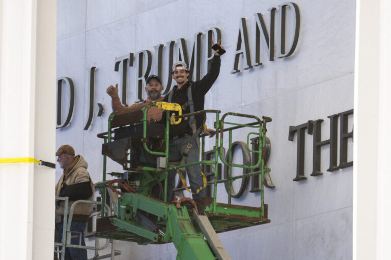 Workers react to the media after updating signage outside the Kennedy Center on Dec. 19, 2025, in Washington, D.C.