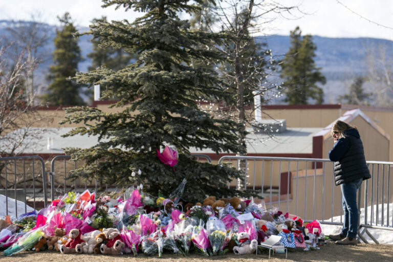 A woman in dark clothes mourns at a makeshift memorial for the victims of a deadly mass shooting that took place at Tumbler Ridge Secondary School, in the town of Tumbler Ridge, British Columbia, Canada. The memorial consists of stuffed animals and flowers at the base of a conifer tree.