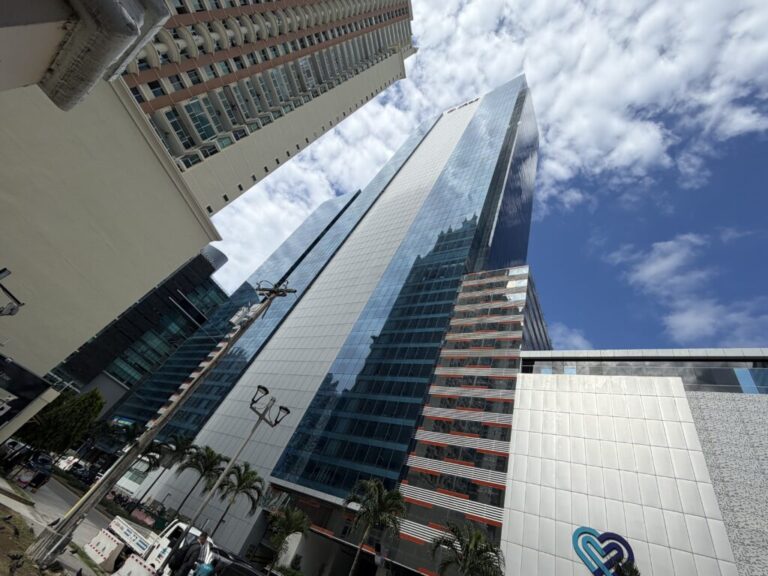 Image of a soaring skyscraper, taken from the ground. The skyscraper is blue and grey and located in the upscale Punta Pacifica neighborhood in Panama City.