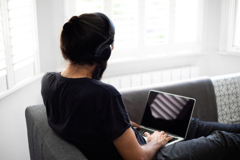 A man with his back to the camera uses a laptop and wears headphones.