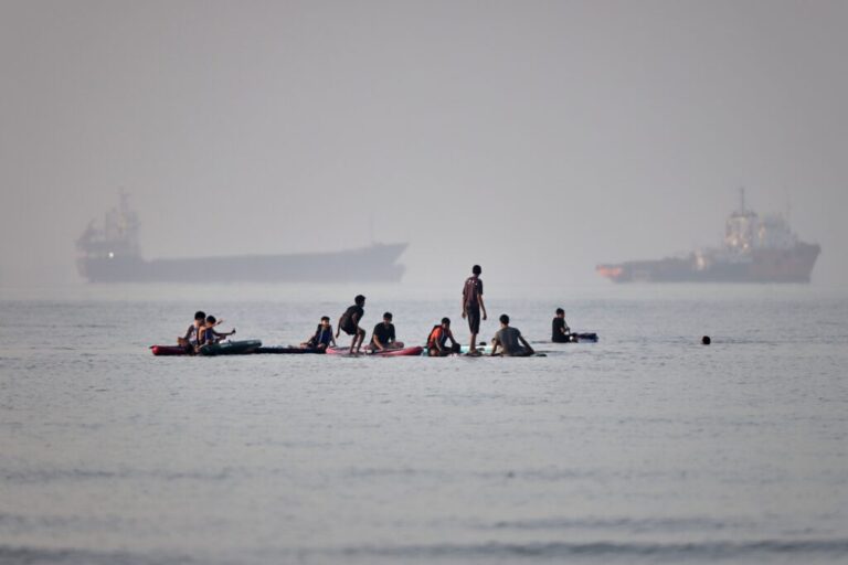 People gather on paddleboards in shallow water as cargo and service vessels are anchored in the Strait of Hormuz off Bandar Abbas, Iran, Monday, June 1, 2026.