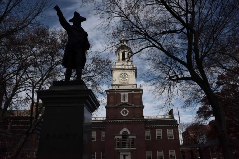 This photo shows Independence Hall in Philadelphia. The brick structure has a bell tower and steeple in the middle.
