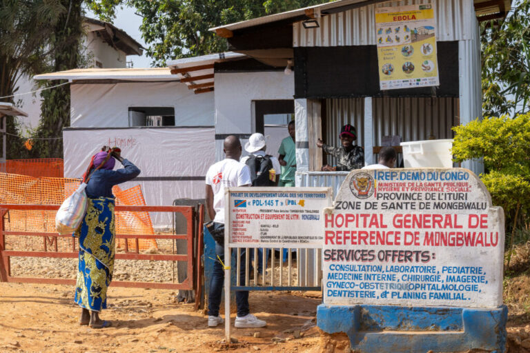 A view of the outside of the Mongbwalu General Referral Hospital in Mongbwalu, Ituri province, Democratic Republic of Congo, on June 15, 2026. Several people are entering the one-story hospital, and a sign out front has the hospital's name in French, along with a list of services offered.