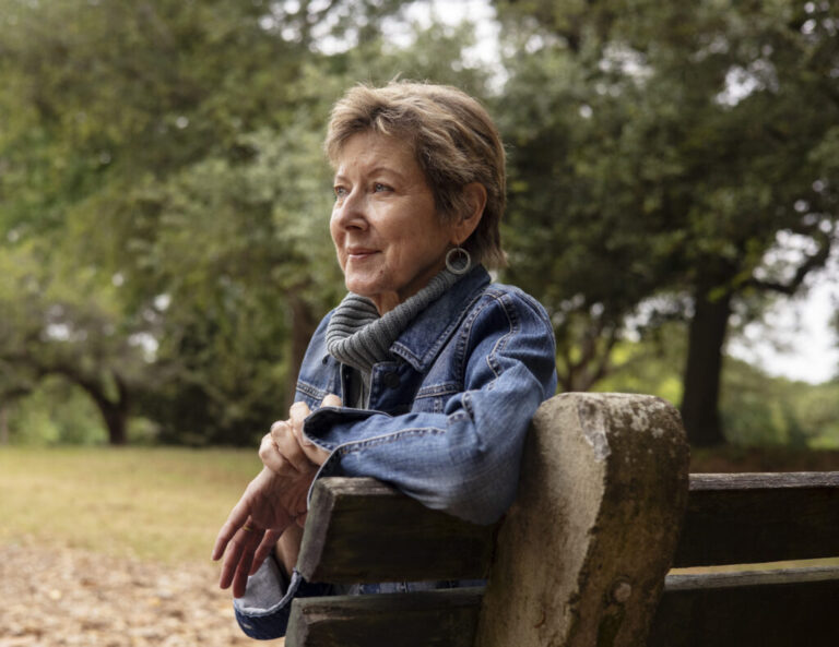 Vicky Stinson, a youthful looking 65-year-old, is pictured in profile, sitting on a part bench.