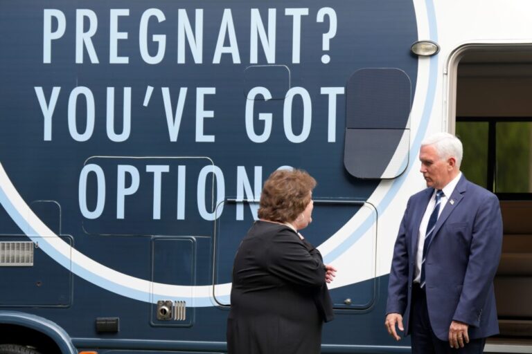 Former VP Mike Pence and Alexa Newman stand next to an RV that has an enormous sign that says,