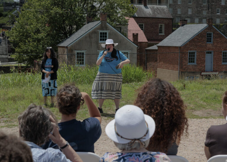 Former National Park Ranger Melissa Dalley, 49, seen here holding a microphone in front of a crowd, speaks during the America 433+ teach-in at Harpers Ferry National Historic Park on June 19, 2026.