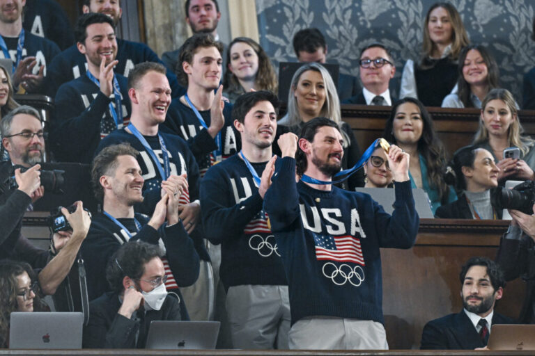 Members of the U.S. men's Olympic ice hockey team stand, with Connor Hellebuyck in front holding up his gold medal.