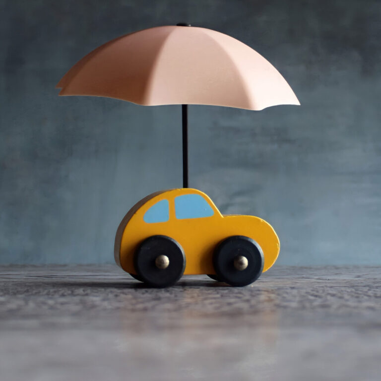 Image of a toy umbrella over a toy car, with a gray background.