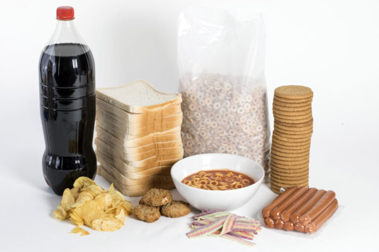 White bread, soda, crackers, cereal, canned spaghetti, hot dogs, chicken nuggets, chips and candy are pictured.