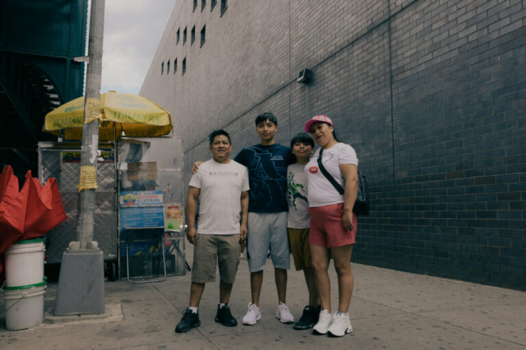 Juan David Iza, center-right, and his mother Lida Iza, right, pose for a portrait with their family along Roosevelt Avenue and 99 Street, as residents navigate the bustling avenue in Queens, New York, U.S., on Sunday, June 7, 2026. CREDIT: José A. Alvarado Jr. for NPR, @josealvarado