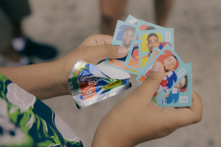 Juan David Iza, opens a sticker pack of Panini World Cup players along Roosevelt Avenue and 98 Street, as residents navigate the bustling avenue in Queens, New York, U.S., on Sunday, June 7, 2026. CREDIT: José A. Alvarado Jr. for NPR, @josealvarado