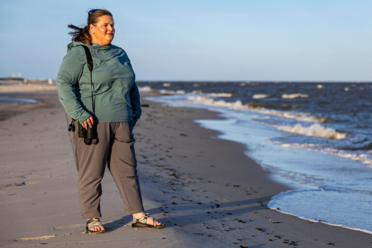 Brittney Brown, a biologist with Florida's Fish and Wildlife Conservation Commission, stands at the beach in Pass Christian, Miss., on June 4. She has binoculars and is wearing a green windbreaker and khakis.