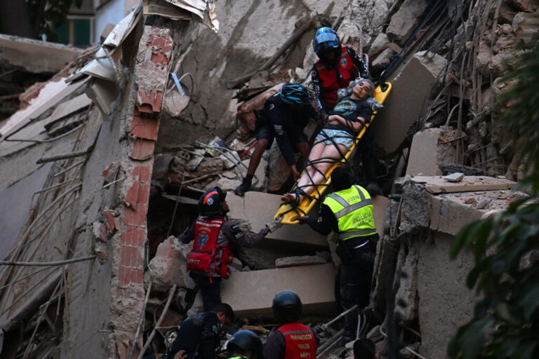 Rescue workers carry a person on a stretcher out of a collapsed building.