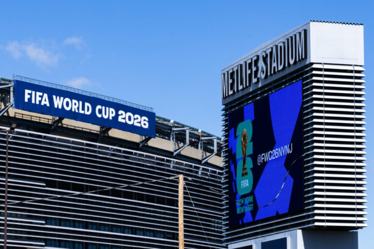 This photo shows the exterior of the MetLife Stadium in East Rutherford, New Jersey. A blue banner at the top edge of the stadium says: