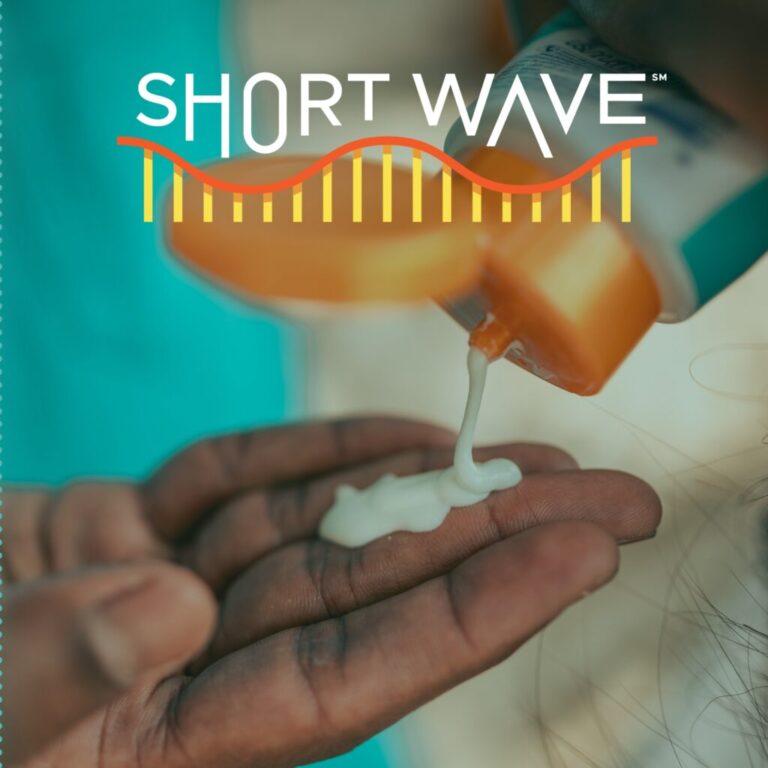 A dark skinned hand squeezes sunscreen from a white and teal plastic tube with an orange top into their hand. At the very right hand side of the image a sliver of the back of someone's head is visible, someone with longer dark hair. In the left half of the image in the blurred background is a what looks to be a teal shirt. The image is beneath the words Short Wave, in white letters at the top of the image. The words are above half of a yellow and orange cartoon wave.