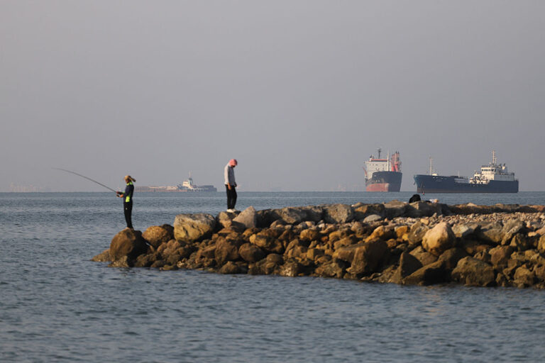 In this picture obtained from Iran's ISNA news agency on June 8, 2026, residents fish from the shore as cargo and commercial vessels lie at anchor in the Strait of Hormuz off Bandar Abbas on June 8, 2026.