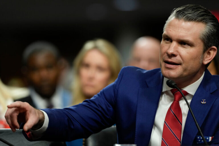 Secretary of Defense Pete Hegseth is shown at his confirmation hearing wearing a blue jacket and red tie.