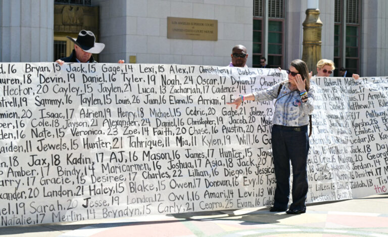 Mary Rodee, whose 15-year-old son died by suicide, points to a banner listing victims' names outside Los Angeles Superior Court.
