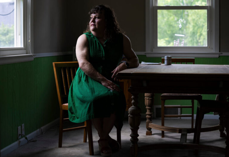 Suzanne Swierc, a health educator at Ball State University, sits at a table while looking out a window behind her. She is wearing a green dress.