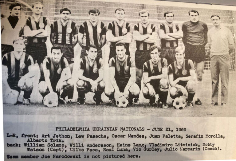 This black-and-white photo shows members of the Philadelphia Ukrainian Nationals soccer team posing for a photo. They are in two rows: one row of members standing in the back and one row of members squatting on the ground in front. Text beneath the photo says: