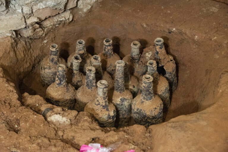 Roughly a dozen bottles in a dirt pit.