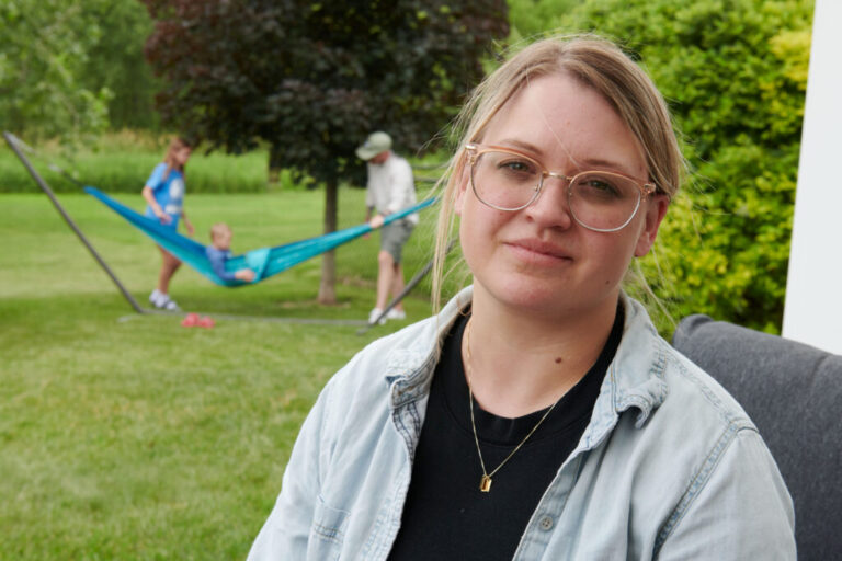 Amber Petersen sits in the backyard of her parents’ home in Iowa City, Iowa on Sunday, June 14, 2026. Petersen lives in Mason City, Iowa with her husband and three children. (Cliff Jette for NPR)