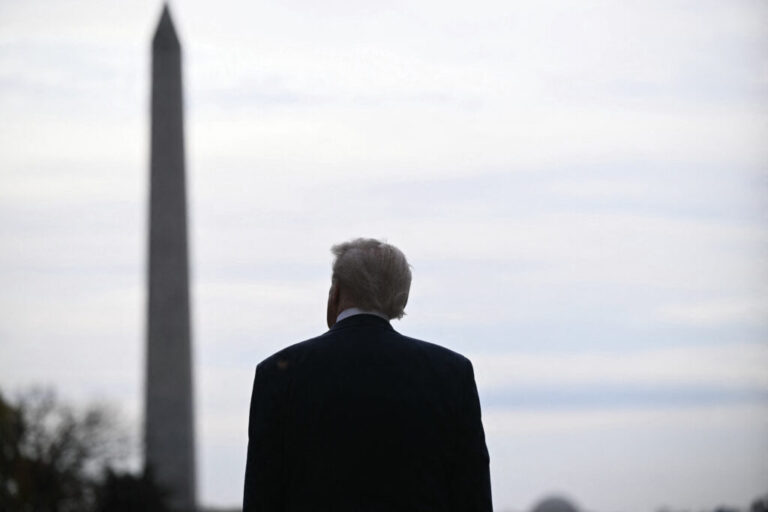 This photo shows President Trump standing outdoors with his back to the camera. The Washington Monument rises in the background.
