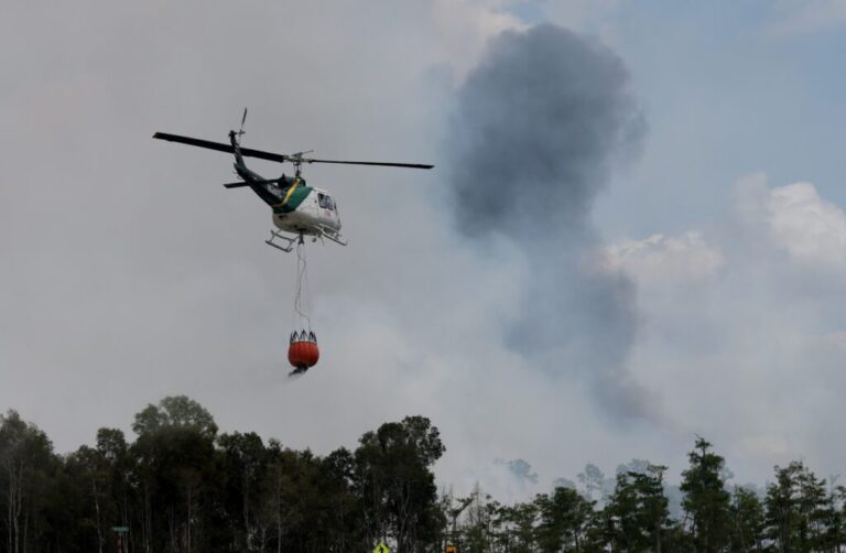 A Florida Forest Service firefighter's helicopter prepares to dump a bucket load of water on a wildfire on April 14, 2026, in Naples, Florida. Conditions in the area are conducive to wildfires due to the lack of rain, causing drought conditions.