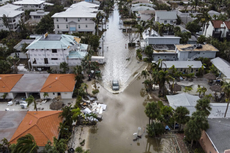 A high-angle photograph of a vehicle driving on a flooded street after Hurricane Milton, in Siesta Key, Florida, on October 10, 2024, after the monster weather system sent tornadoes spinning across the state and flooded swaths of the Tampa Bay area.