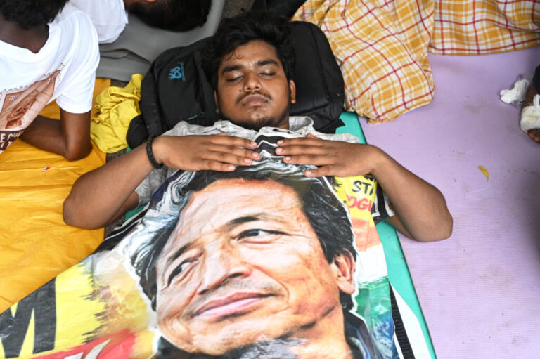 A reclining protestor covers himself with a banner printed with a portrait of Sonam Wangchuk, a prominent activist who was forcefully transferred to a hospital by the police as he staged a hunger strike in support of a movement led by Cockroach Janta Party, at a protest in New Delhi, India, Wednesday, July 22, 2026.