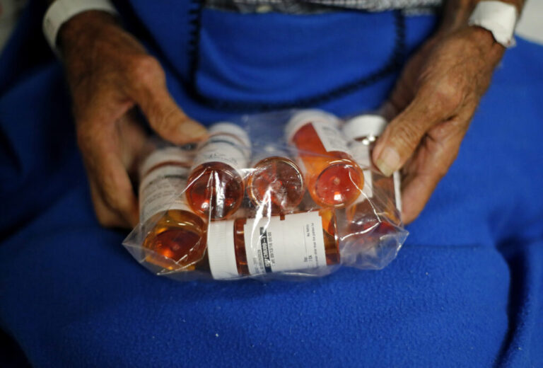 A person holds a plastic bag filled with prescription pill bottles.