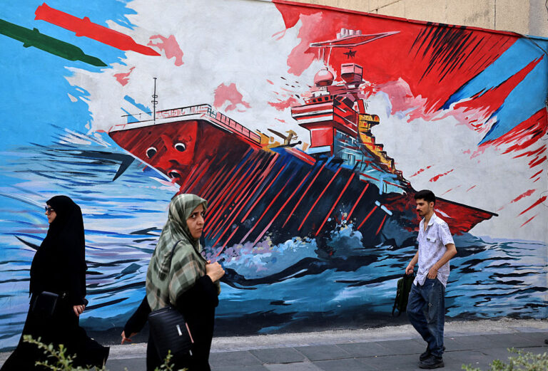 Commuters walk past a wall mural along the street in Tehran on July 21.