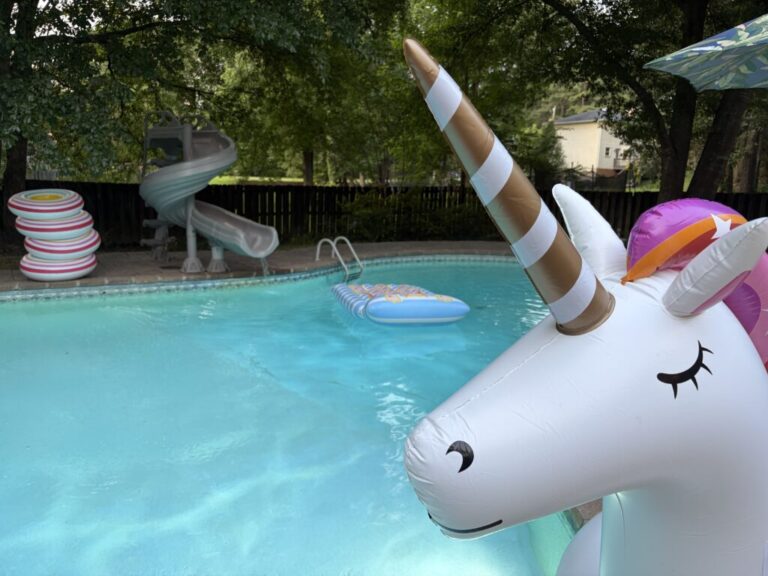 A swimming pool with a slide and an inflatable unicorn, raft and floatation tubes.
