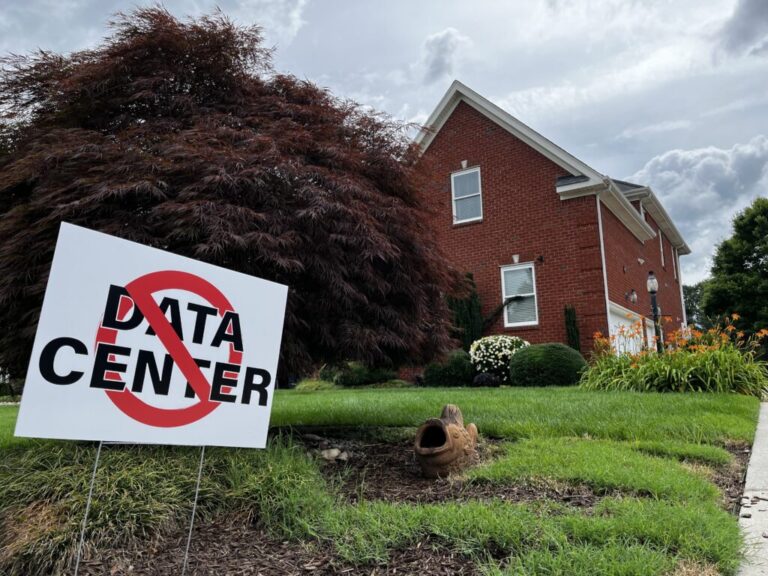 This photo shows a white yard sign that says in all caps,