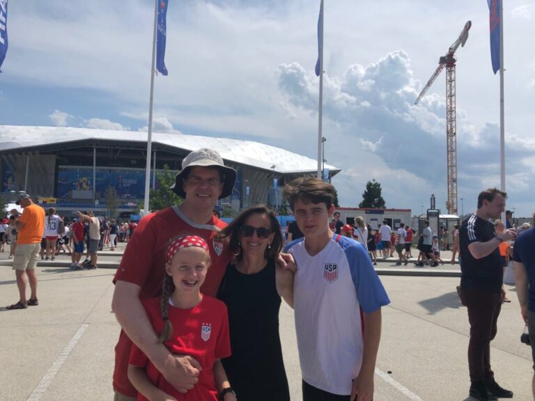 Mike Trucano (left) and his family pose in front of the stadium hosting the final for the 2019 Women's World Cup in Lyon, France,.