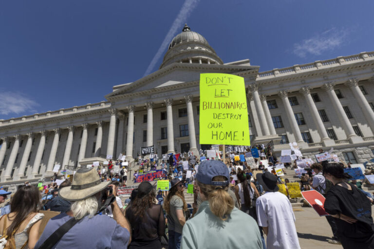 Protesters hold signs in front the of the Utah State Capitol building to oppose the construction of the Stratos data center on May 23, 2026 in Salt Lake City, Utah. The most prominent sign in the photo reads: