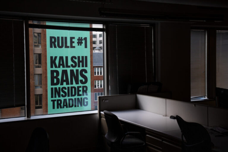 Viewed through the window of an office building, a giant banner for the prediction market platform Kalshi hangs on the outside of a building across the street on April 1. The banner says in all capital letters: