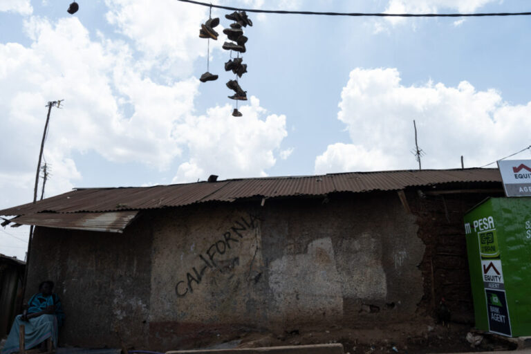 Shoes hang from power lines above a neighborhood building with a rusty metal roof.