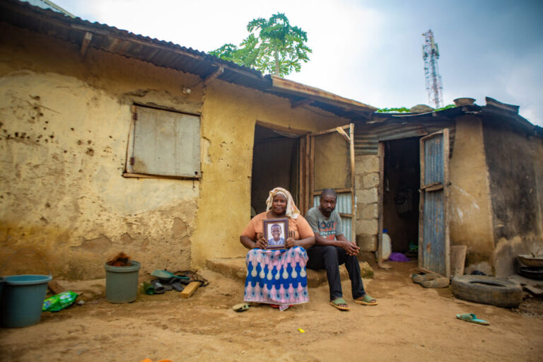 Asibi Garba and her husband, Yakubu Garba, sit outside their home holding a framed portrait of their son, Ibrahim, who died from typhoid.