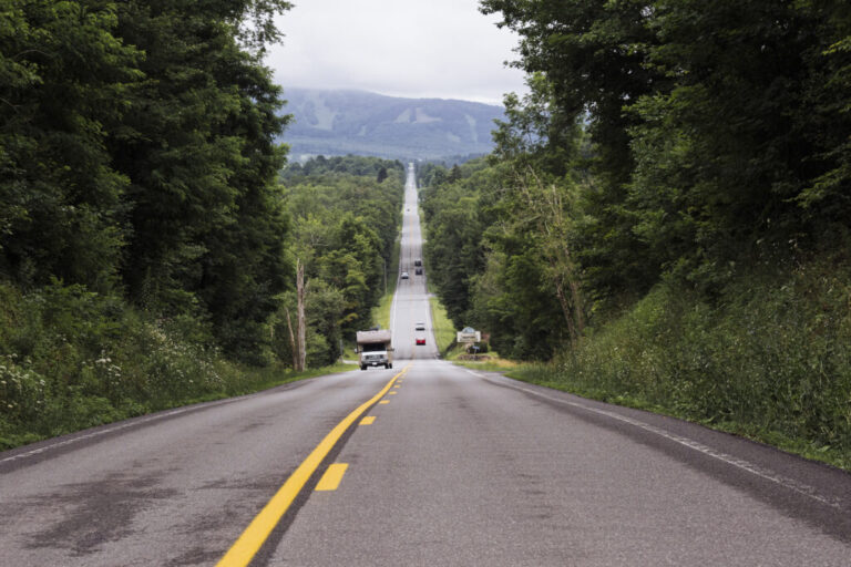 A two-lane road stretches downhill into the distance with trees on both sides.