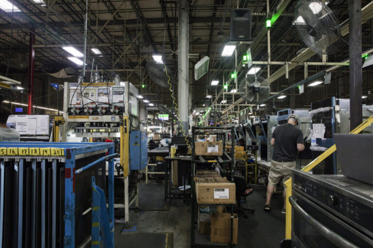 An assembly-line worker installs parts on an oven at a large factory.